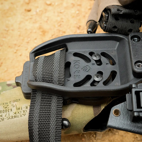 Close-up of a black tactical belt with a visible brand logo on a camouflage background.