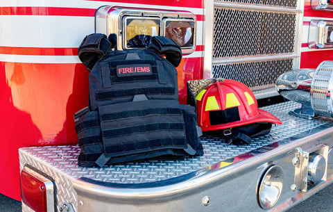 Safety gear: A tactical ballistic vest and a red firefighter helmet perched on a fire truck bumper