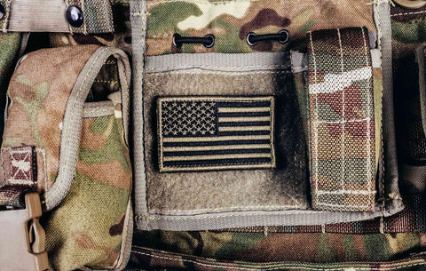 Close-up of multi-camouflaged soldier vest pouches, illustrating what one might consider when buying a magazine pouch, with an American flag patch visible.