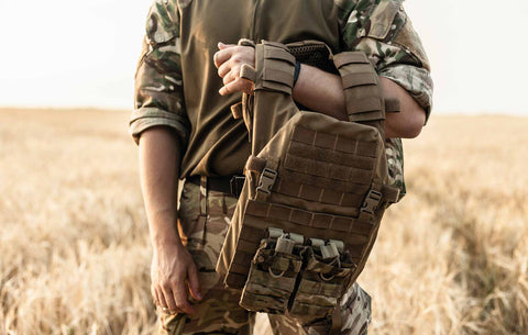 Soldier in full tactical attire standing in an open field with a focus on the bulletproof vest, signifying readiness and defense.