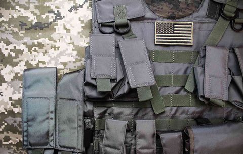 An overhead photo of a tactical military bulletproof vest with an American flag badge lying on a camouflage cloth background.