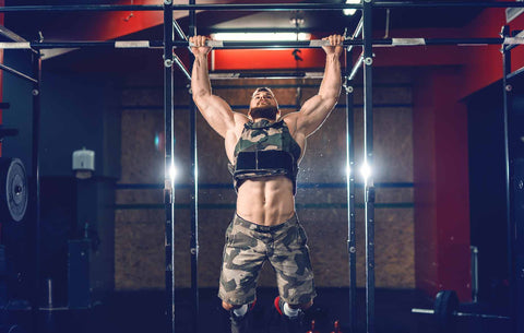 A man doing pull-ups in military style weighted vest in crossfit gym