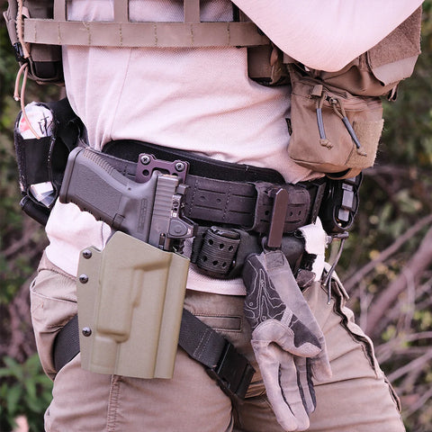 Person wearing tactical gear with a gun holster and gloves on a blurred natural background