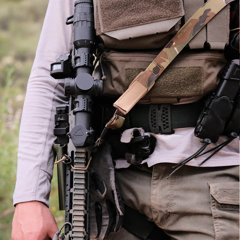 Person wearing tactical gear with a rifle and backpack in an outdoor setting