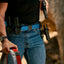 Person wearing a blue belt with multiple holsters and a gun, outdoors.