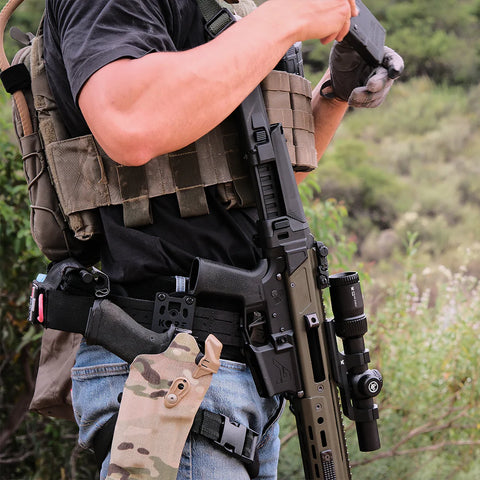 Person wearing tactical gear with a rifle in an outdoor setting