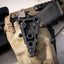 Black tactical mount on a camouflage surface with a gun in the background