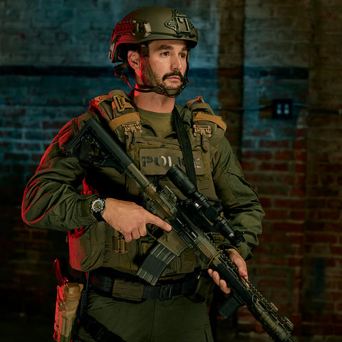 Person in tactical gear holding a rifle against a brick wall background