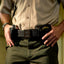 Person wearing a beige shirt and green pants with a belt and gun holster.