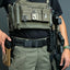 Person wearing tactical gear with a focus on a green utility belt and pouches.
