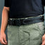 Person wearing a black belt with camouflage pattern on green pants against a gray background
