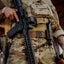 Person in camouflage military uniform holding a rifle with tactical gear.