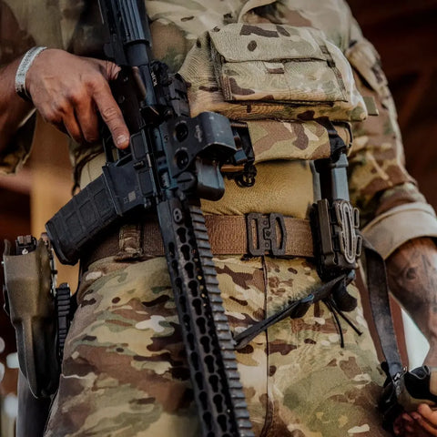 Person in camouflage military uniform holding a rifle with tactical gear.