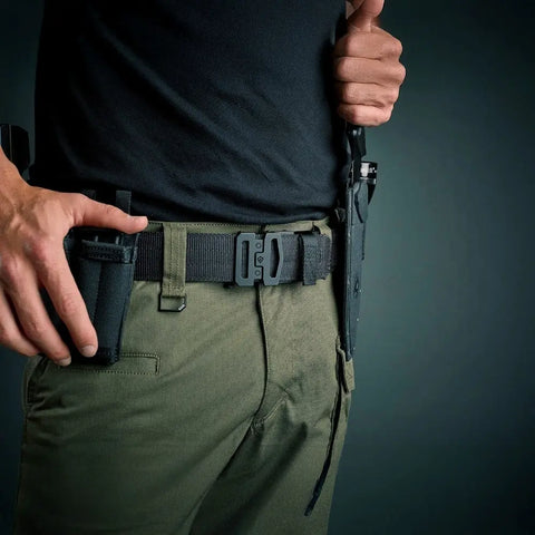 Person wearing green pants and a black shirt with tactical gear on a dark background